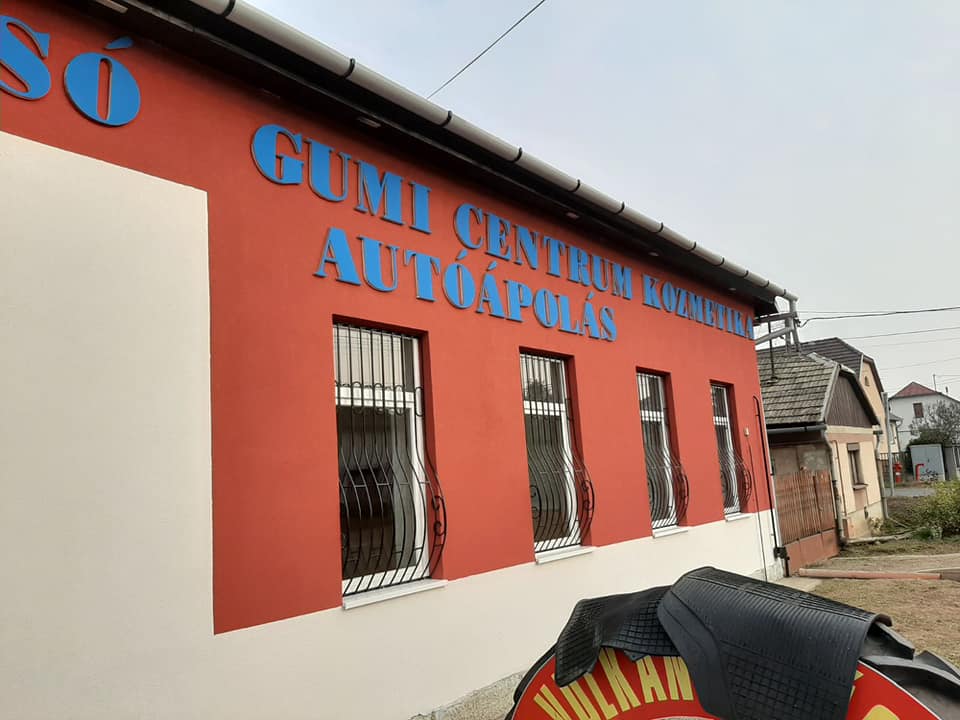 A CZÉ-MO Autócentrum piros épülete kék felirattal: gumi centrum, kozmetika, autóápolás